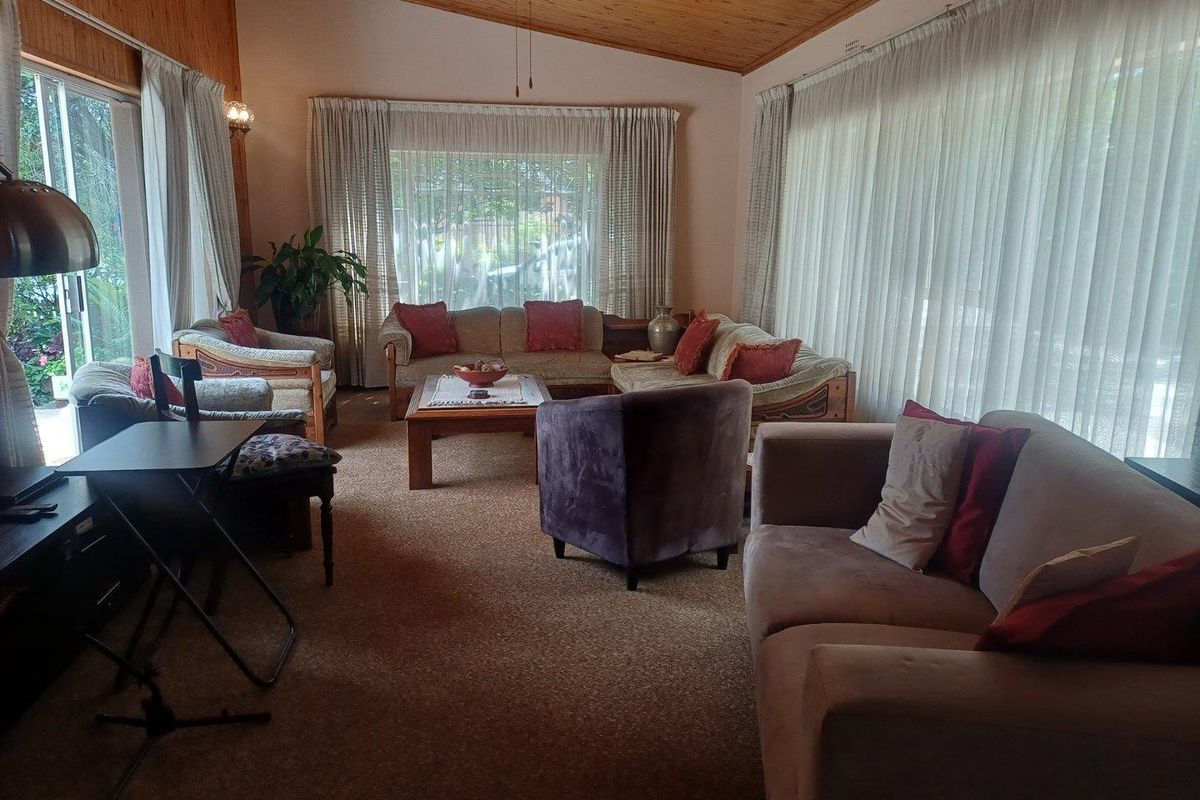 Spacious living room featuring a vaulted timber ceiling, large windows with natural light, and carpeted flooring.