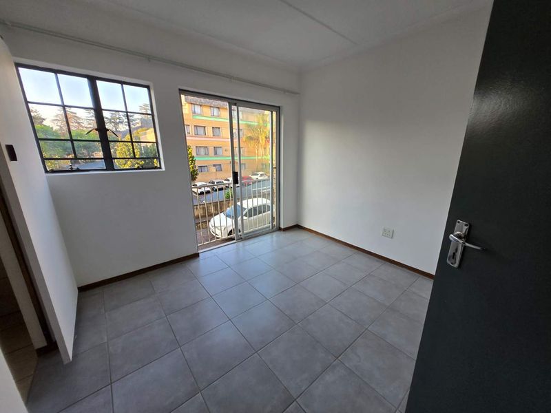 A bright, empty bedroom featuring neutral tiled flooring, a sliding glass door leading to a balcony, and large windows providing natural light.
