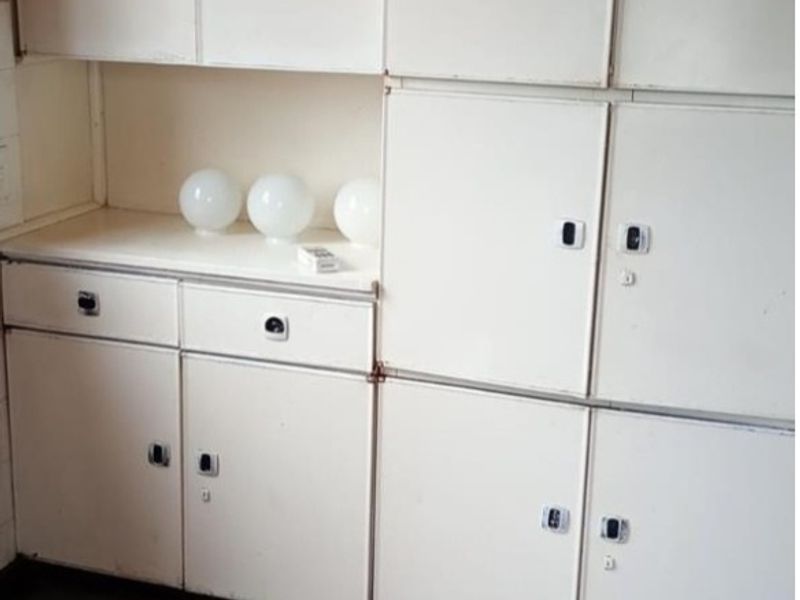A dated kitchen area featuring original built-in cabinetry and retro-style vinyl tile flooring, offering significant potential for modernization and renovation.