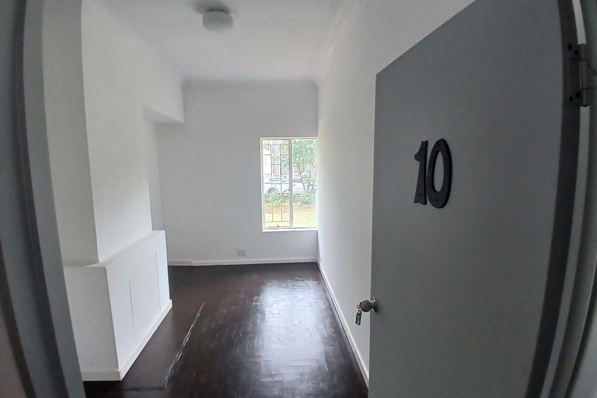A view into an empty room featuring dark parquet flooring, white walls, and a window with security bars.
