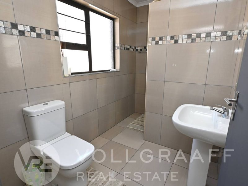 A clean, tiled bathroom featuring a pedestal washbasin, a toilet, and a walk-in shower area with neutral wall tiles.