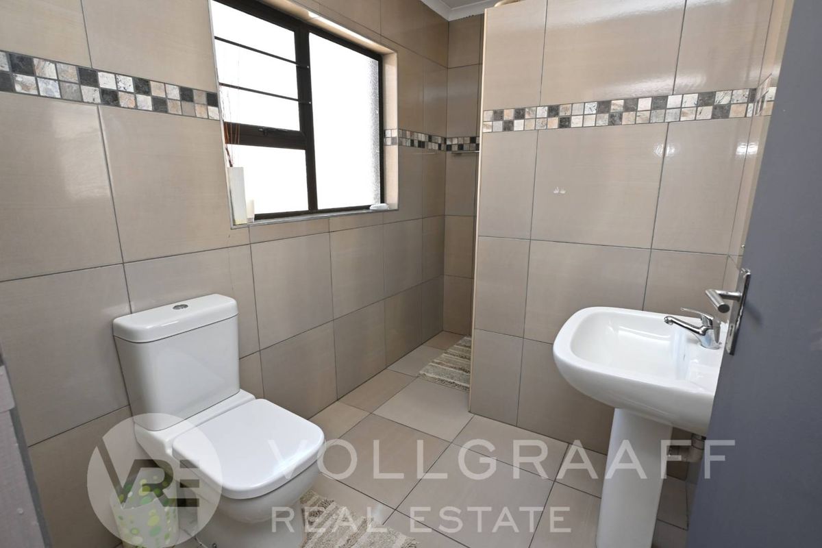 A clean, tiled bathroom featuring a pedestal washbasin, a toilet, and a walk-in shower area with neutral wall tiles.