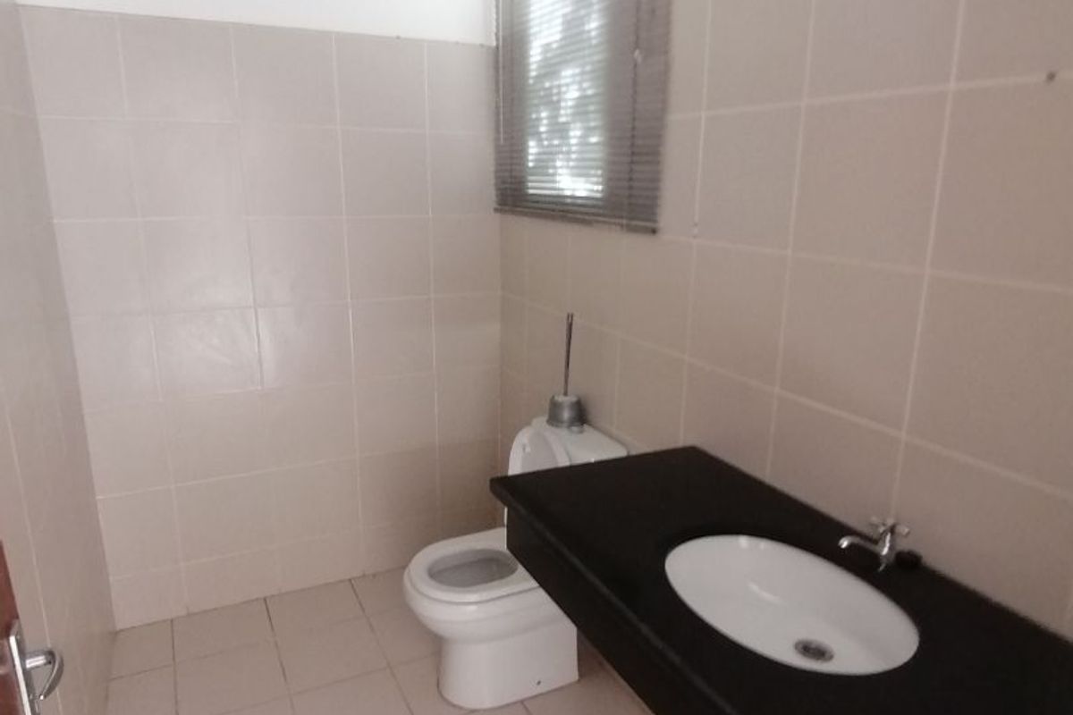 A functional bathroom featuring a built-in vanity with a basin and a standard toilet, finished with neutral wall and floor tiling.