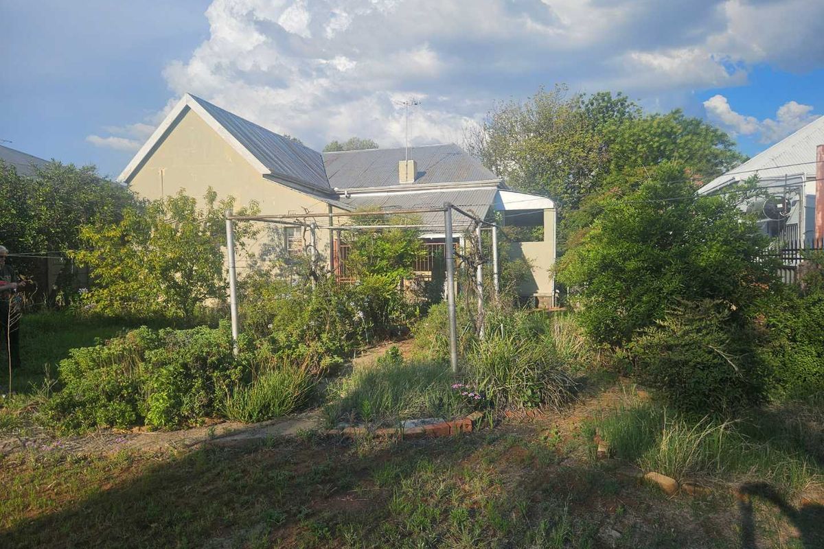 A view of the rear exterior of the house, featuring a large, overgrown garden and a metal pergola structure.