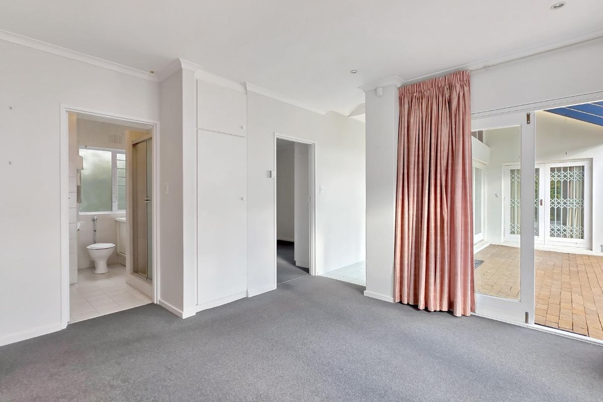Spacious bedroom featuring neutral carpeting, built-in storage, an en-suite bathroom, and direct access to an outdoor patio area through glass sliding doors.