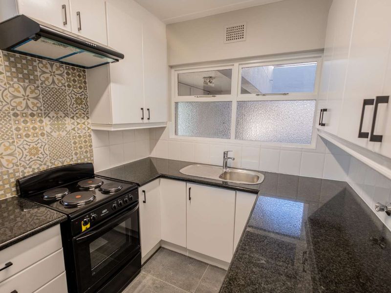 A clean, modern kitchen featuring white cabinetry, dark granite countertops, a built-in electric stove with extractor fan, and decorative tiled backsplash.