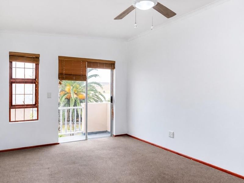 An empty bedroom featuring neutral carpeting, a ceiling fan, and a sliding glass door providing access to a private balcony.
