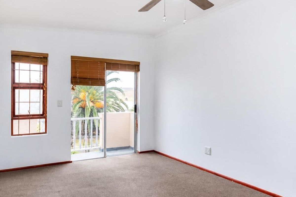 An empty bedroom featuring neutral carpeting, a ceiling fan, and a sliding glass door providing access to a private balcony.