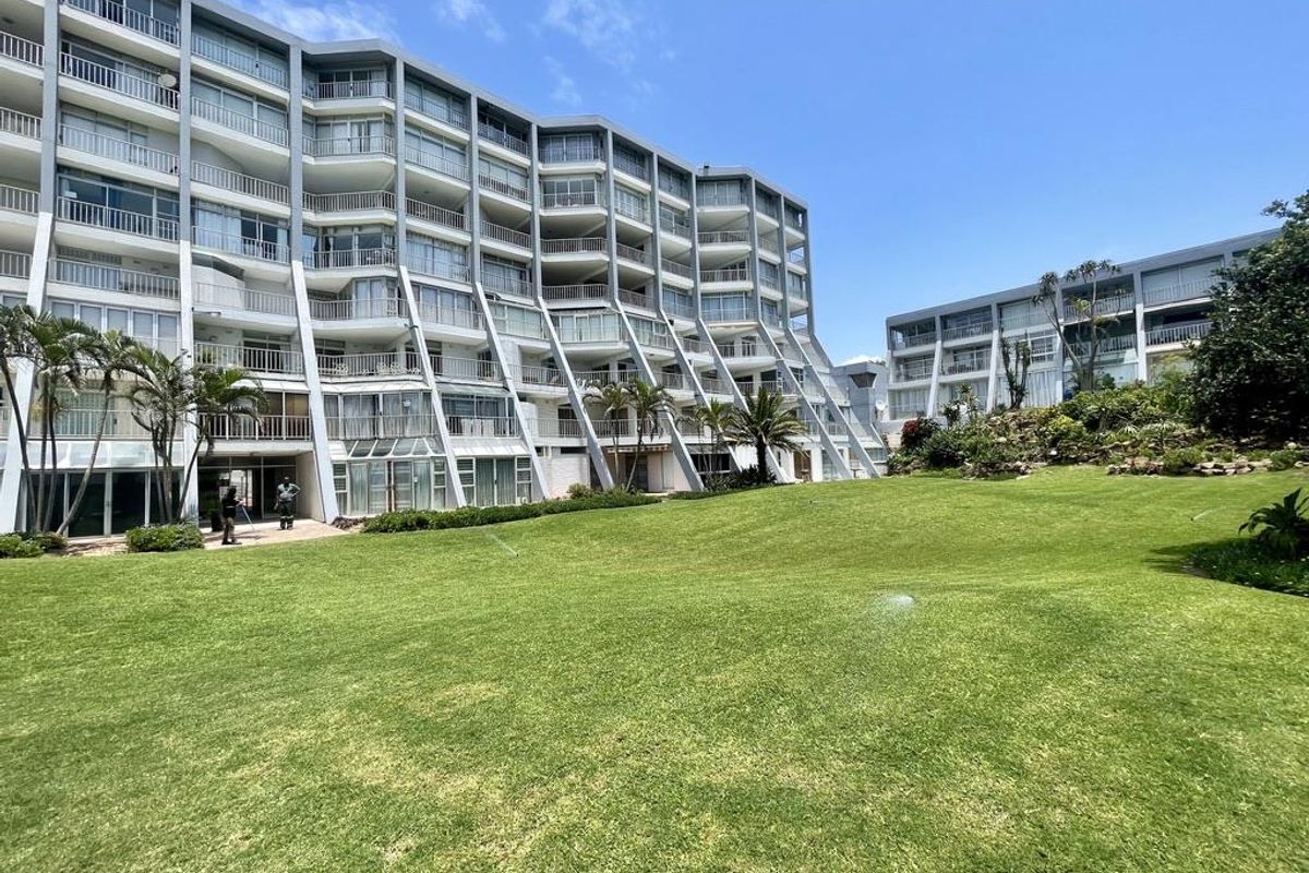 Exterior view of a multi-story apartment complex featuring private balconies and a well-maintained communal lawn area.