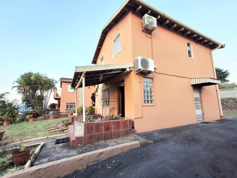 Exterior view of a two-story house featuring a tiled porch, security gate, and wall-mounted air conditioning units with an adjacent driveway.