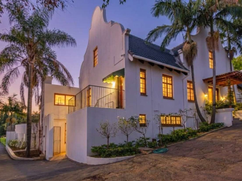 A striking Cape Dutch style residence featuring a distinctive gabled facade, paved driveway, and elegant architectural detailing set against a twilight sky.