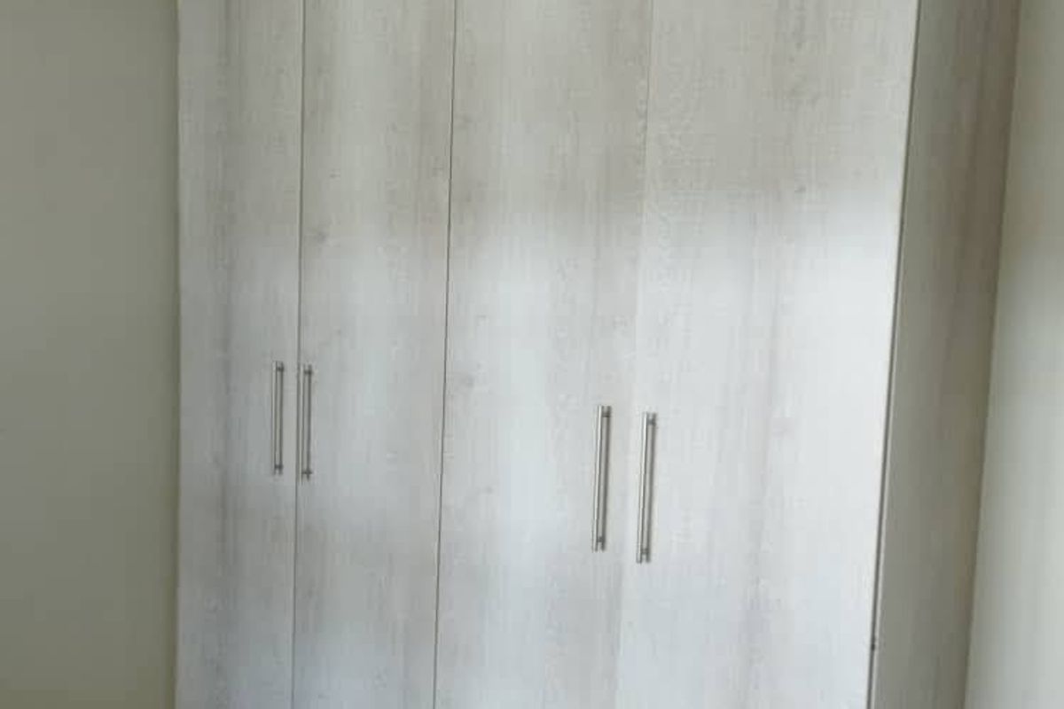 A bedroom featuring modern, light-toned built-in cupboards with sleek handles and wood-look flooring.