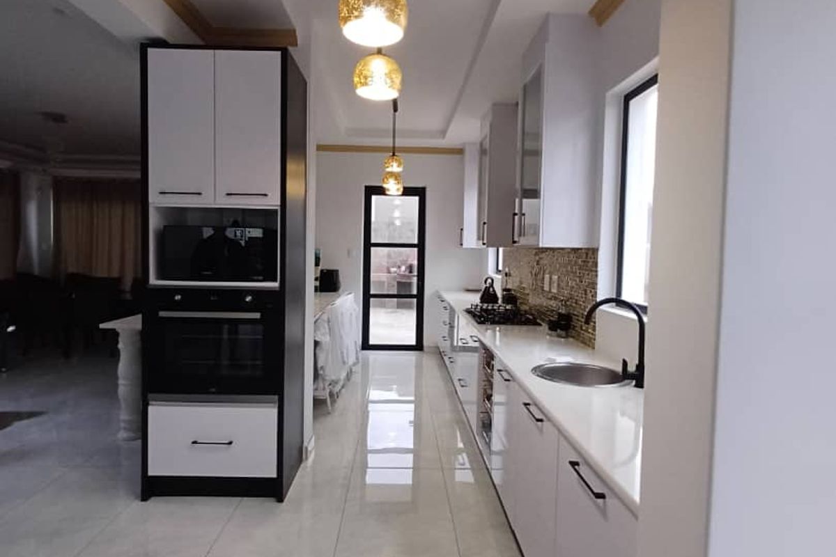 Modern galley-style kitchen featuring sleek white cabinetry, stone countertops, integrated oven, gas hob, and contemporary pendant lighting with polished floor tiles.