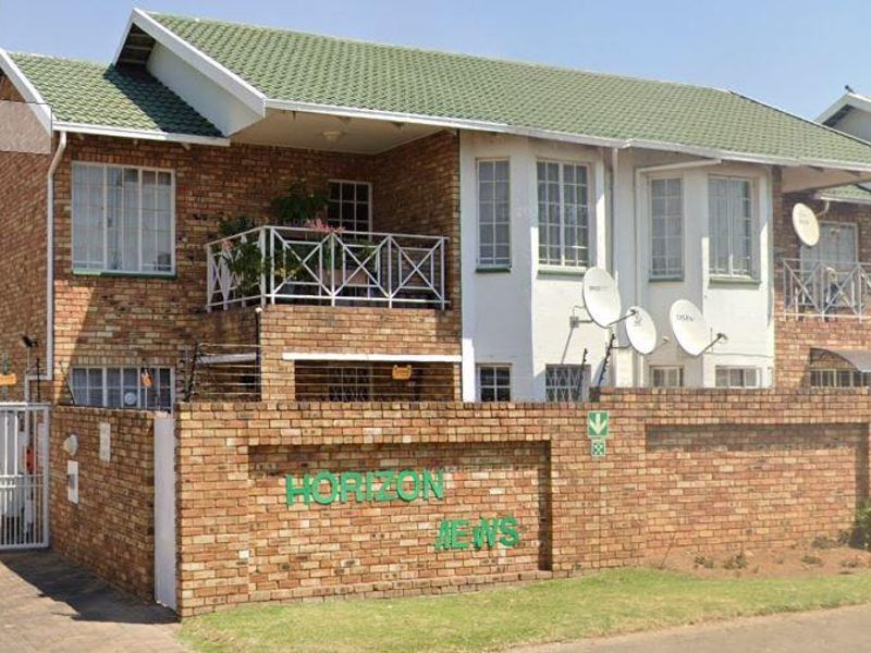 Front elevation of a face brick townhouse complex featuring a tiled roof, balcony, and secure perimeter wall with electric fencing.