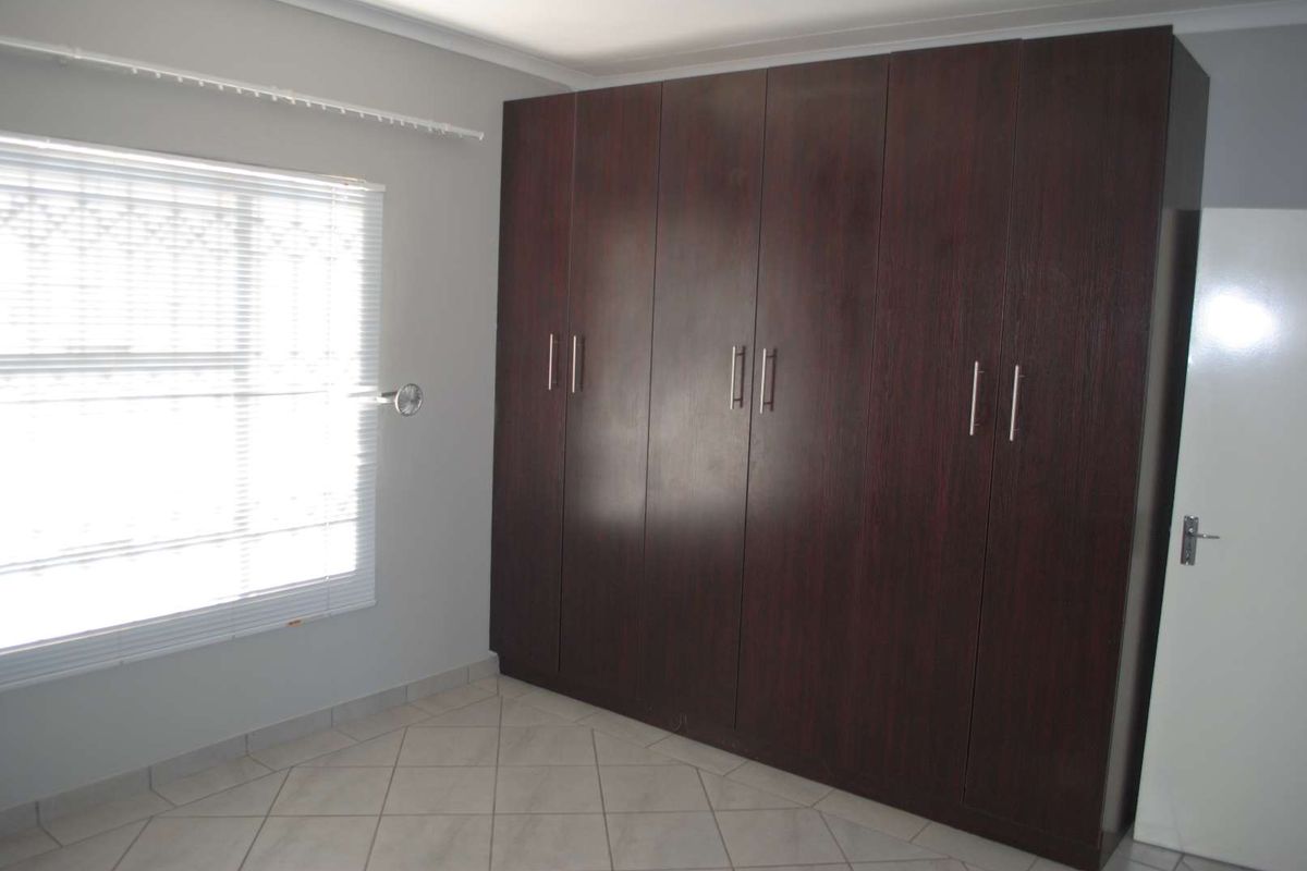 A bedroom featuring built-in dark wood cabinetry, tiled flooring, and a window with fitted blinds.