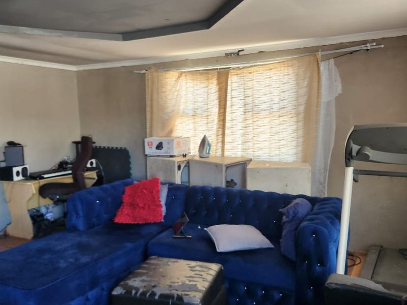 A living room featuring tiled flooring and a recessed ceiling detail, currently requiring wall finishing and cosmetic updates to improve the overall aesthetic.