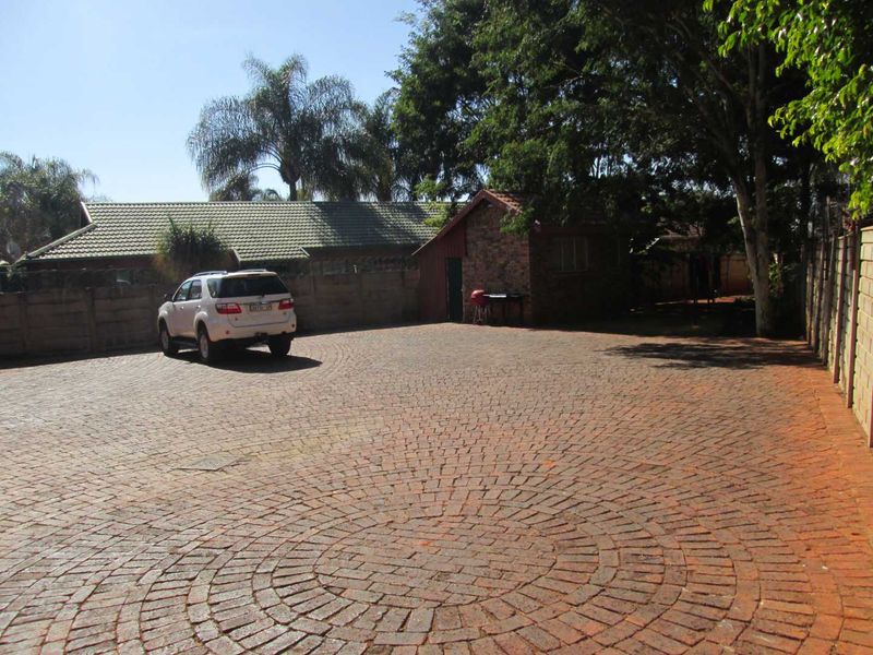A spacious rear exterior area featuring extensive brick paving, a boundary wall, and a small outbuilding structure.