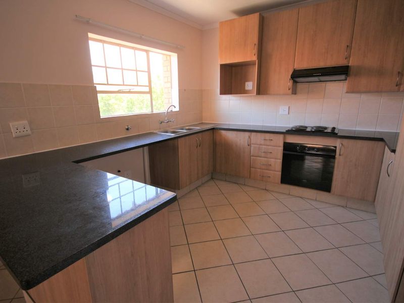A clean, functional kitchen featuring laminate cabinetry, granite countertops, built-in oven, electric hob, and tiled flooring.
