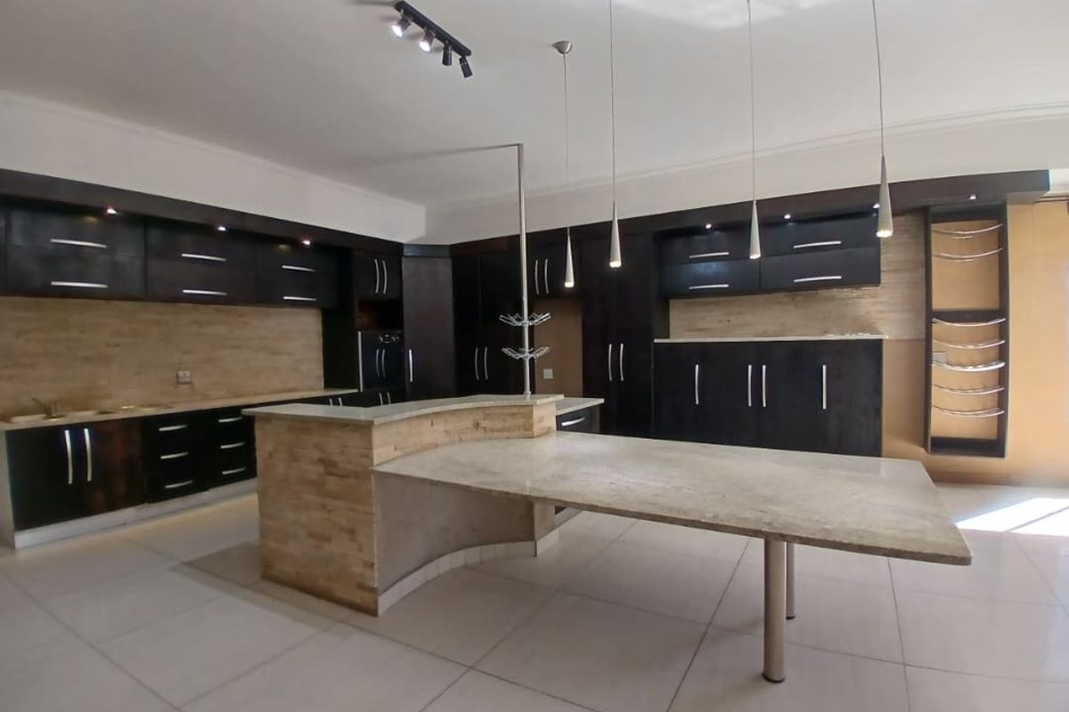 Spacious modern kitchen featuring dark cabinetry, stone-clad island with integrated breakfast bar, tiled flooring, and contemporary pendant lighting.