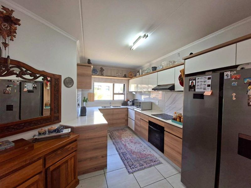 Modern kitchen featuring wood-grain cabinetry, white countertops, integrated appliances, and tiled flooring, offering a functional and well-maintained workspace.