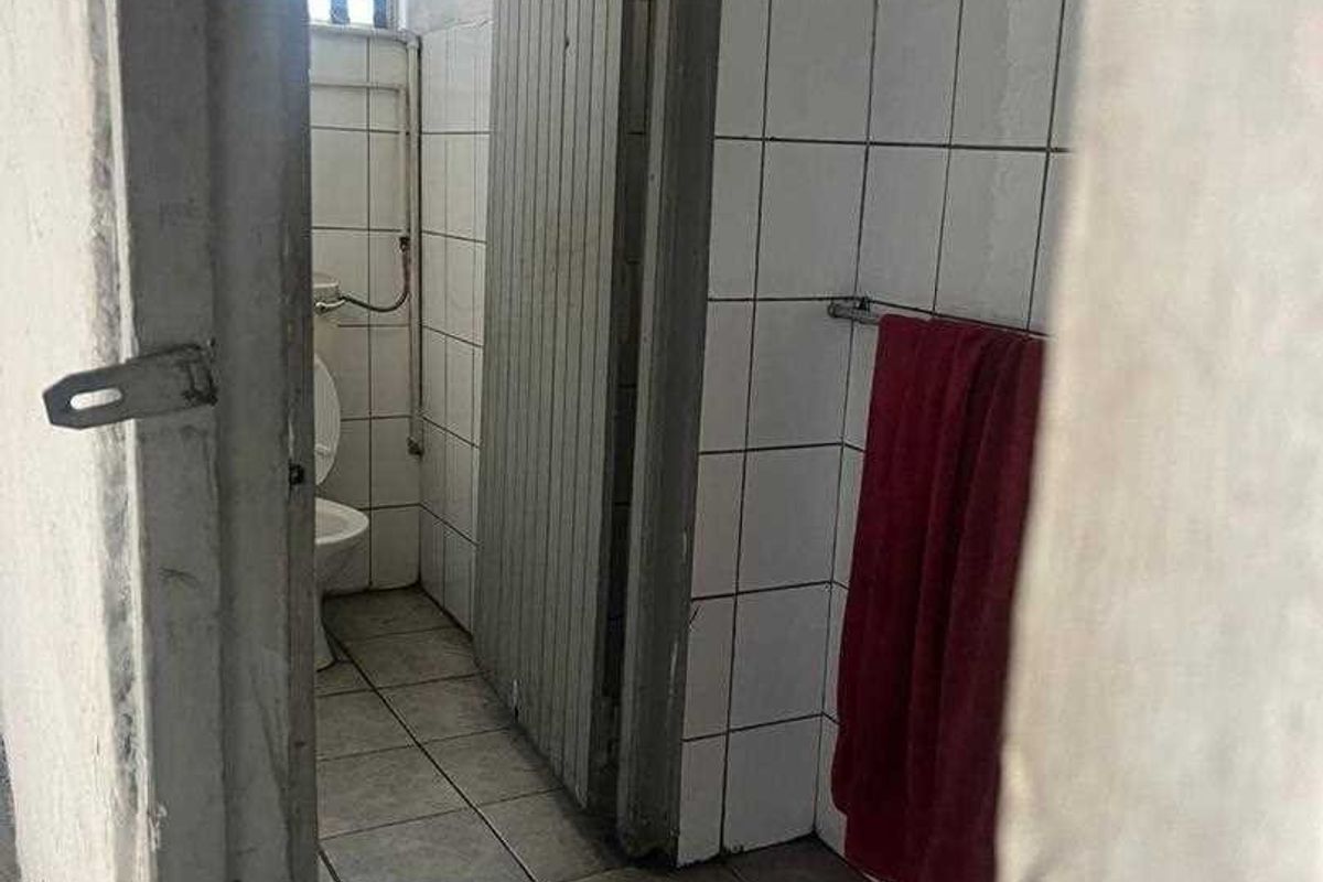 A functional bathroom featuring tiled flooring, wall-mounted towel rail, and a standard toilet fixture, showing signs of wear and dated finishes.