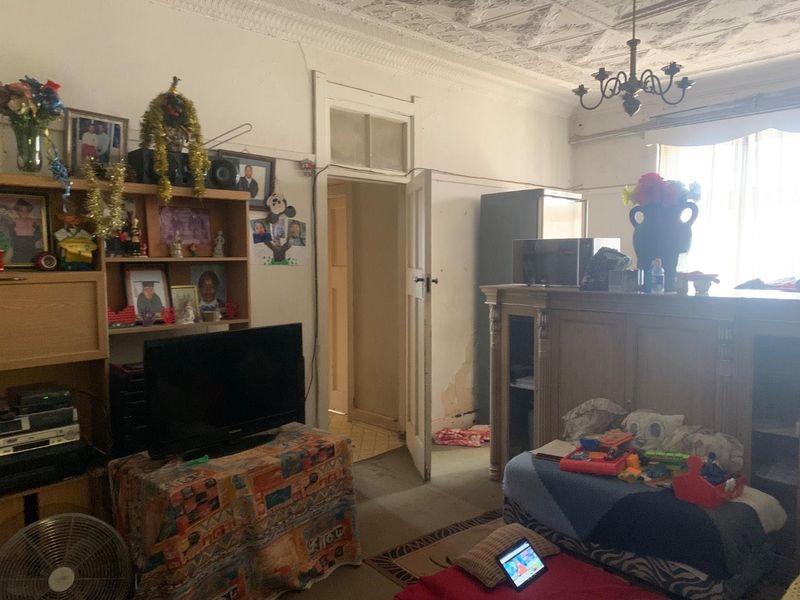 A living room featuring an ornate ceiling, chandelier, and traditional architectural details, currently requiring cosmetic updates and maintenance to the wall finishes.