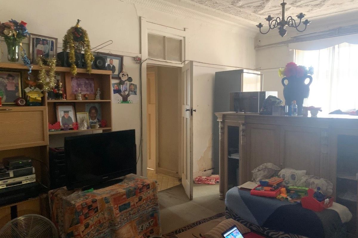 A living room featuring an ornate ceiling, chandelier, and traditional architectural details, currently requiring cosmetic updates and maintenance to the wall finishes.