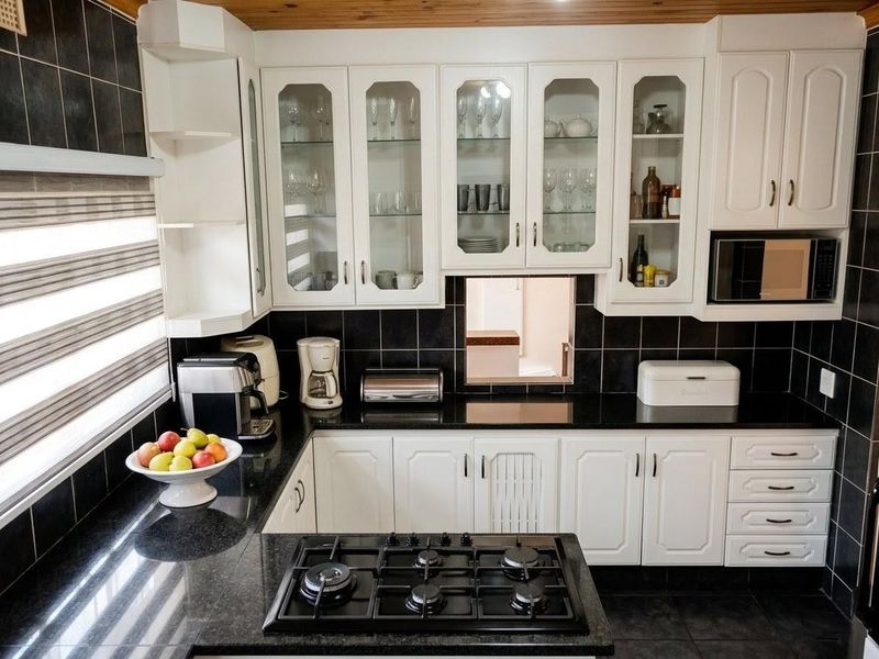 A functional kitchen featuring white cabinetry, black granite countertops, a built-in gas hob, and a timber-paneled ceiling.
