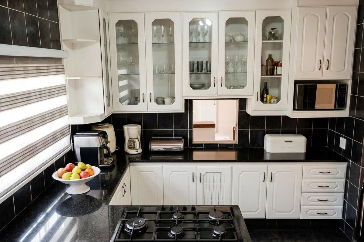 A functional kitchen featuring white cabinetry, black granite countertops, a built-in gas hob, and a timber-paneled ceiling.