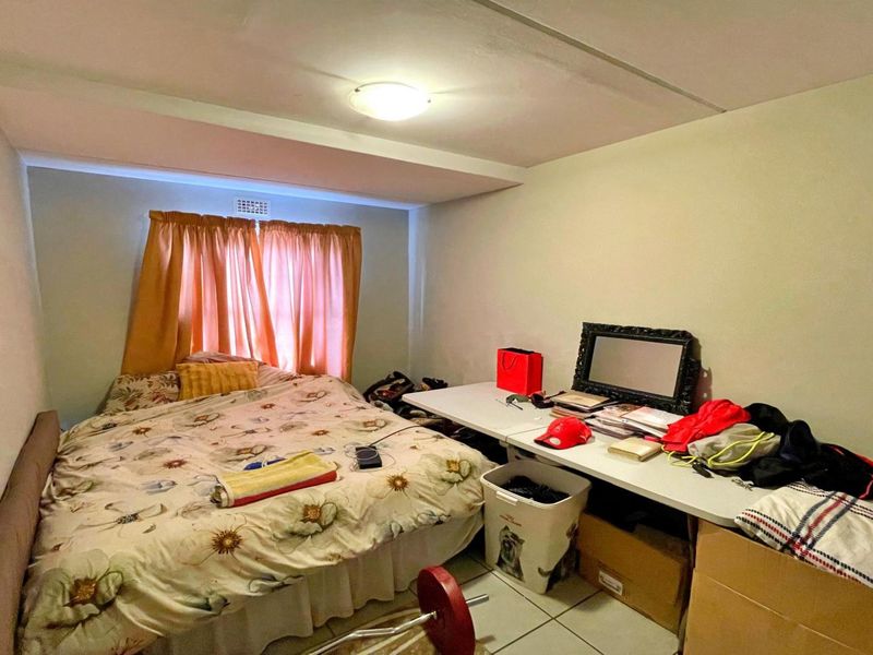 A compact bedroom featuring tiled flooring and a window, currently showing signs of wear including ceiling damage.