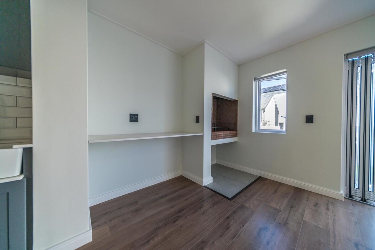 A bright, modern indoor braai area featuring built-in brick fireplace, sleek shelving, and durable wood-look flooring with access to the patio.
