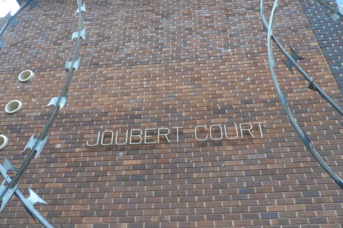 Exterior view of the brick facade of Joubert Court, featuring prominent building signage and security razor wire fencing.