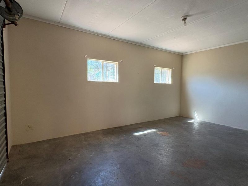 A spacious, empty garage featuring concrete flooring, a roller shutter door, and two windows with security bars, offering a functional utility or storage space.