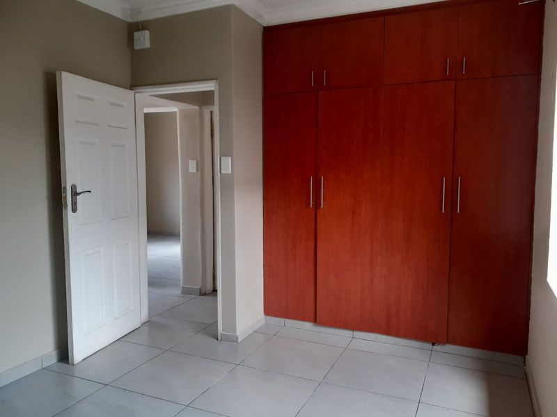 A clean, empty bedroom featuring neutral wall tones, tiled flooring, and floor-to-ceiling built-in wooden cupboards.