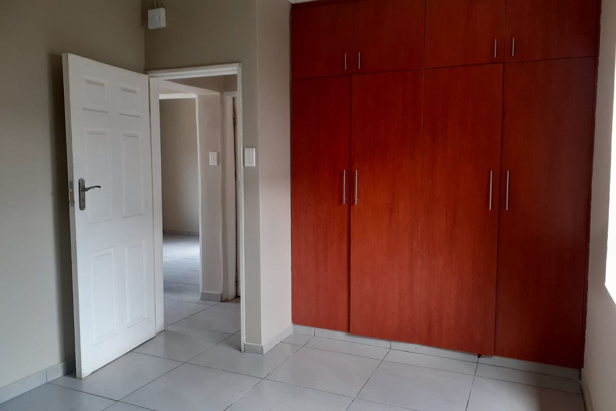 A clean, empty bedroom featuring neutral wall tones, tiled flooring, and floor-to-ceiling built-in wooden cupboards.