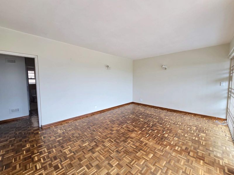 A spacious, empty living room featuring classic parquet flooring, neutral walls, and a sliding glass door leading to an outdoor area.