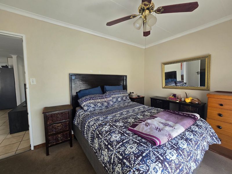 A standard bedroom featuring a ceiling fan, neutral wall finishes, and carpet flooring, offering a functional space ready for cosmetic updates.