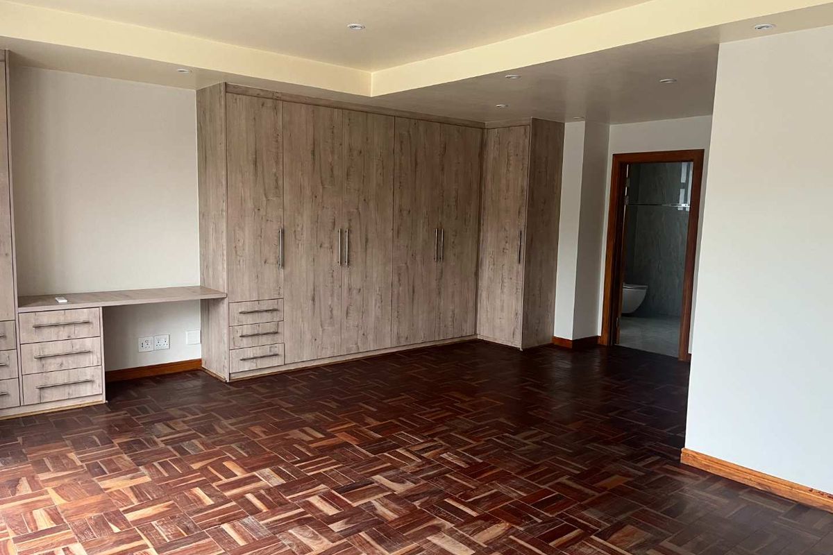 Spacious bedroom featuring polished parquet flooring, extensive built-in wooden cabinetry with an integrated desk, and direct access to an en-suite bathroom.