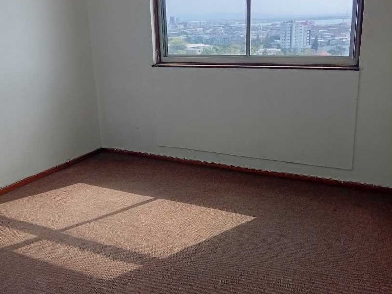An empty bedroom featuring carpet flooring and a large sliding window with views of the surrounding city.