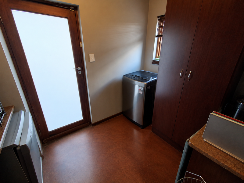 A functional laundry room featuring built-in dark wood cabinetry, a frosted glass exterior door, and durable flooring with space for laundry appliances.
