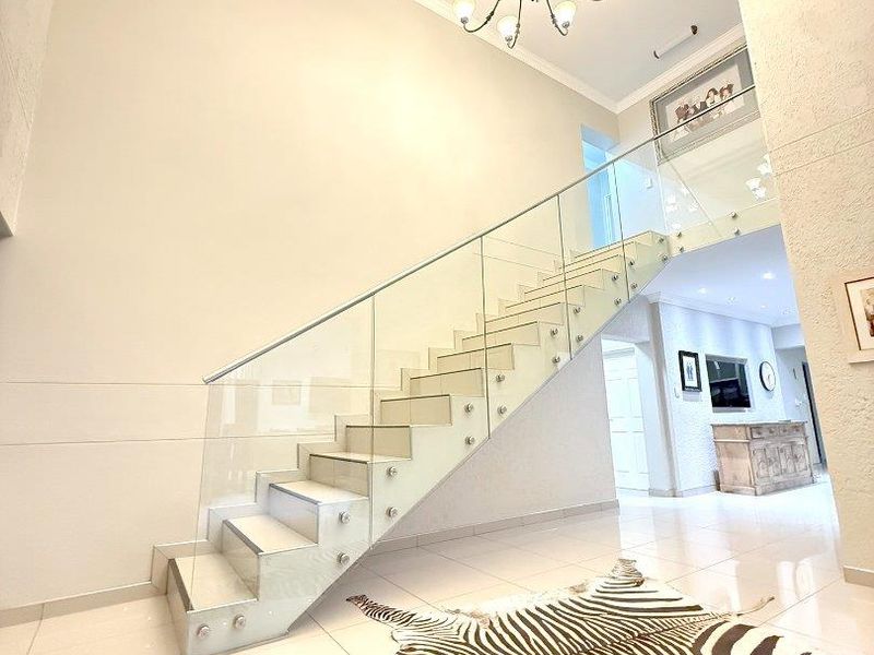 Spacious entrance hall featuring a modern staircase with a glass balustrade, high ceilings, and elegant chandelier lighting.