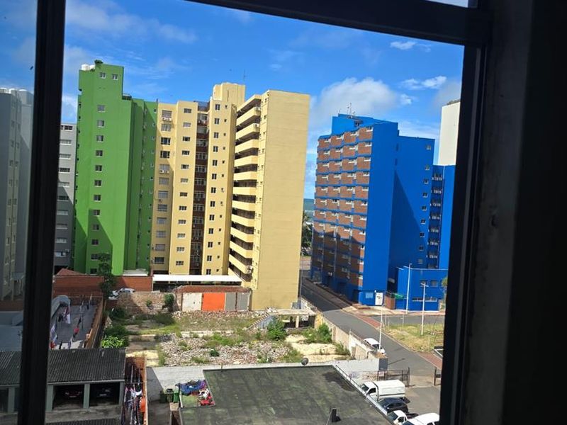 An elevated urban view from an apartment window looking out over neighbouring residential buildings and street infrastructure.