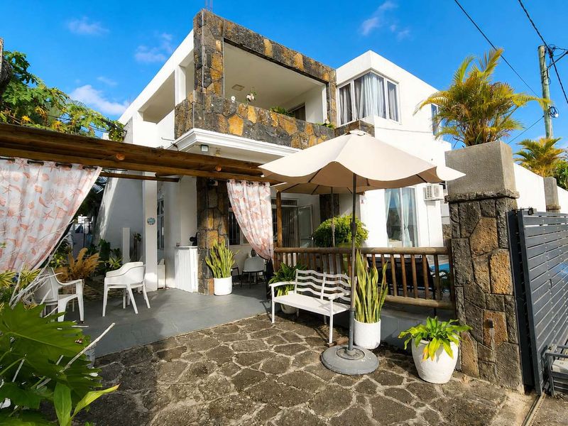 A two-story residential property featuring stone cladding, a timber pergola over a paved patio, and an upper-level balcony.
