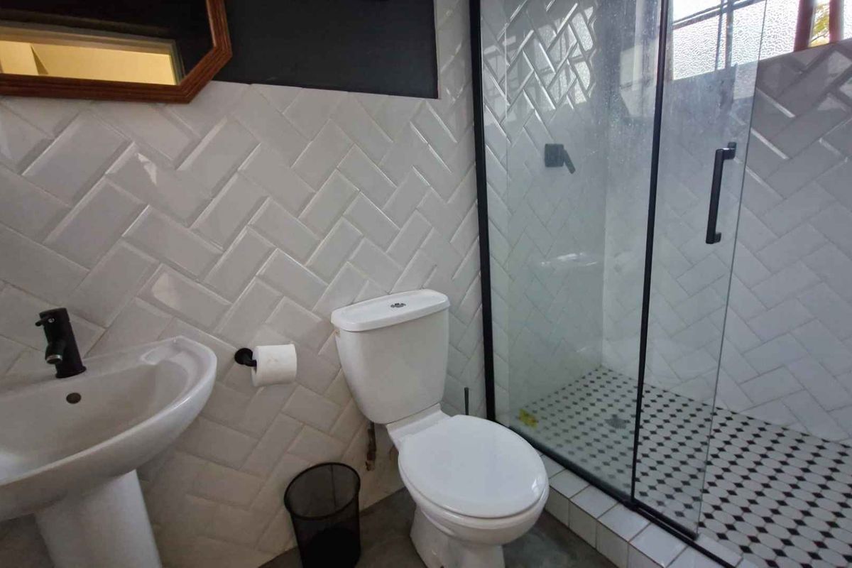 Modern bathroom featuring a glass-enclosed shower, pedestal basin with black fixtures, and stylish herringbone wall tiling.