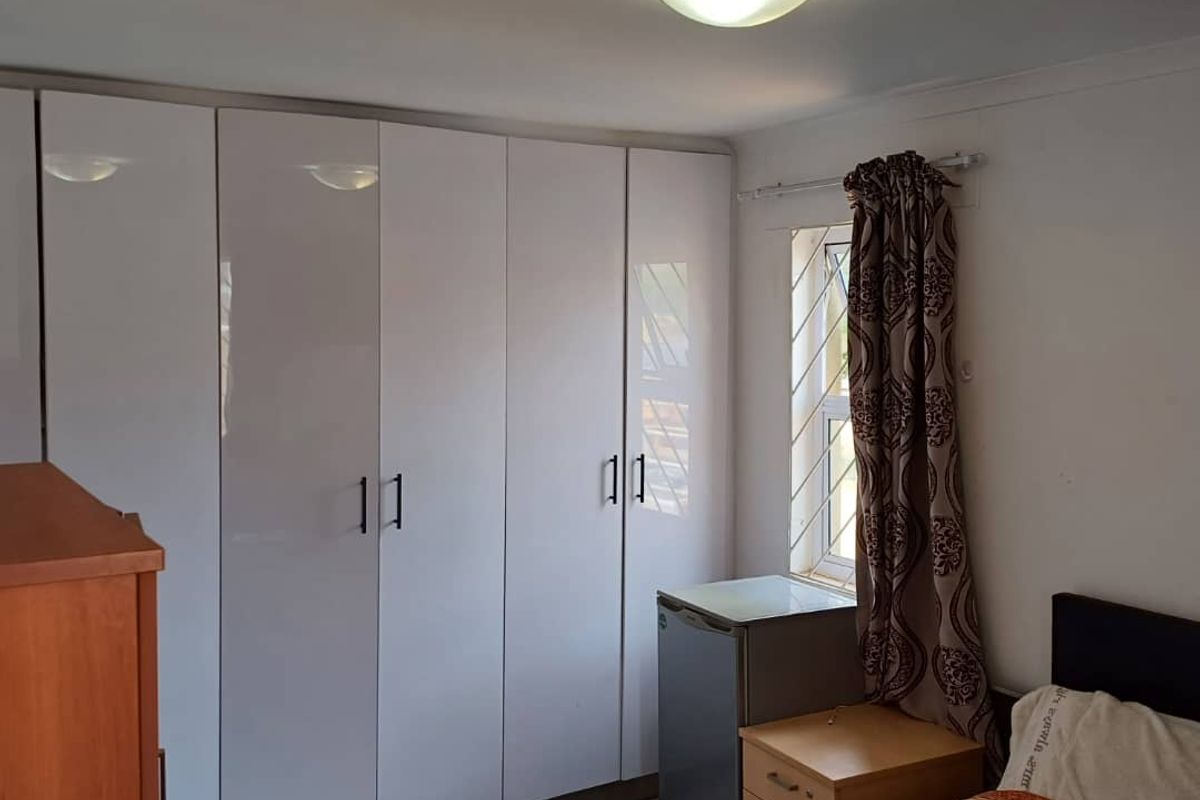 A bedroom featuring white high-gloss built-in wardrobes, tiled flooring, and a window fitted with security bars.