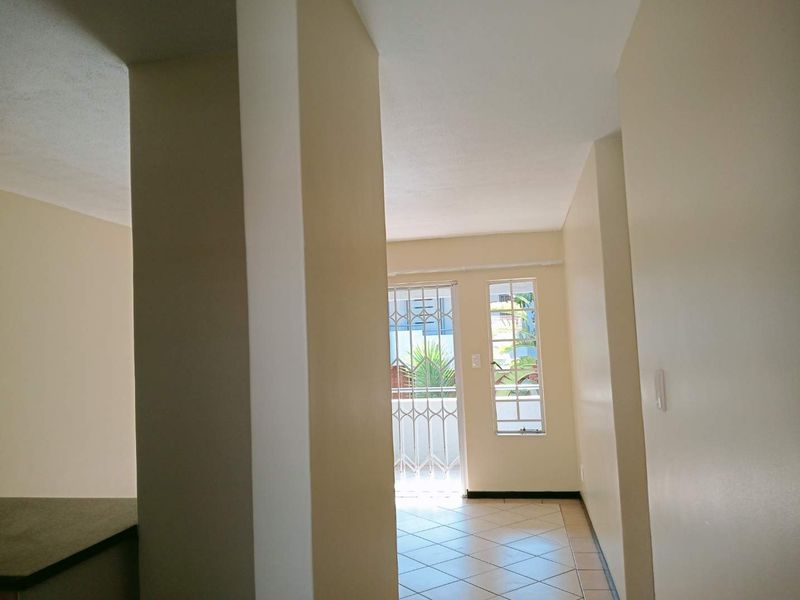 An empty living area featuring tiled flooring, a security gate leading to an outdoor space, and windows with security bars.