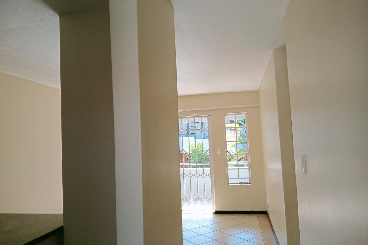 An empty living area featuring tiled flooring, a security gate leading to an outdoor space, and windows with security bars.