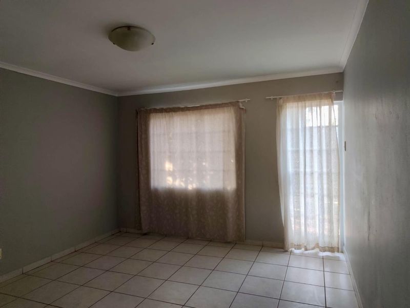 An empty living room featuring neutral tiled flooring, coved cornicing, and natural light provided by a window and a glass-panelled door.