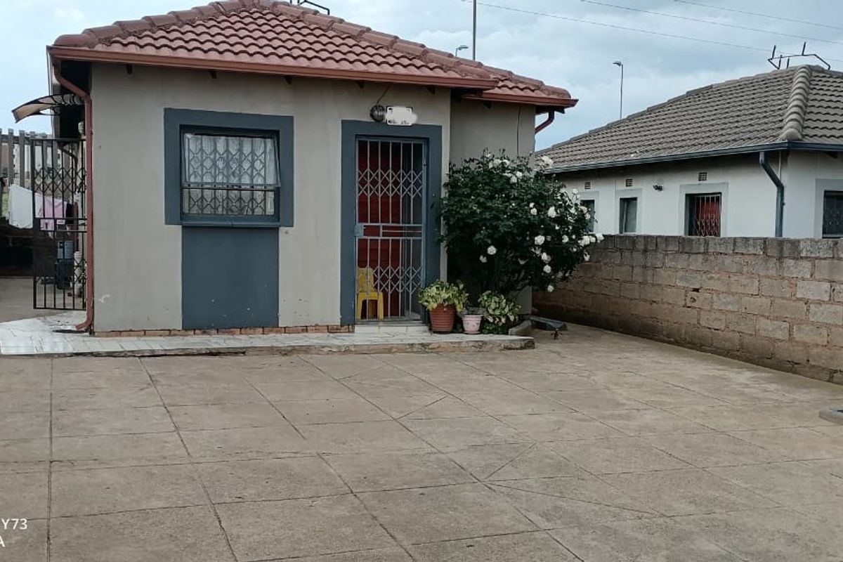 Rear exterior view of a detached house featuring a tiled roof, concrete paved yard, and perimeter boundary walls.