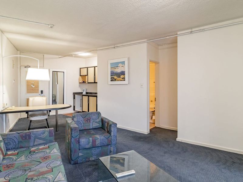 Open plan living area featuring a compact kitchenette with laminate countertops and carpeted flooring throughout, showing dated interior finishes.